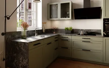 Klassische L‑Küche in Salbeigrün mit Rahmenfronten, dunkler Stein-Arbeitsplatte und großem Fenster; Doppelspüle mit Chromarmatur, Glas-Hängeschränke, schwarze Schräghaube, Induktionsfeld mit Kessel und Wok, Kräutertopf, Holzfußboden.